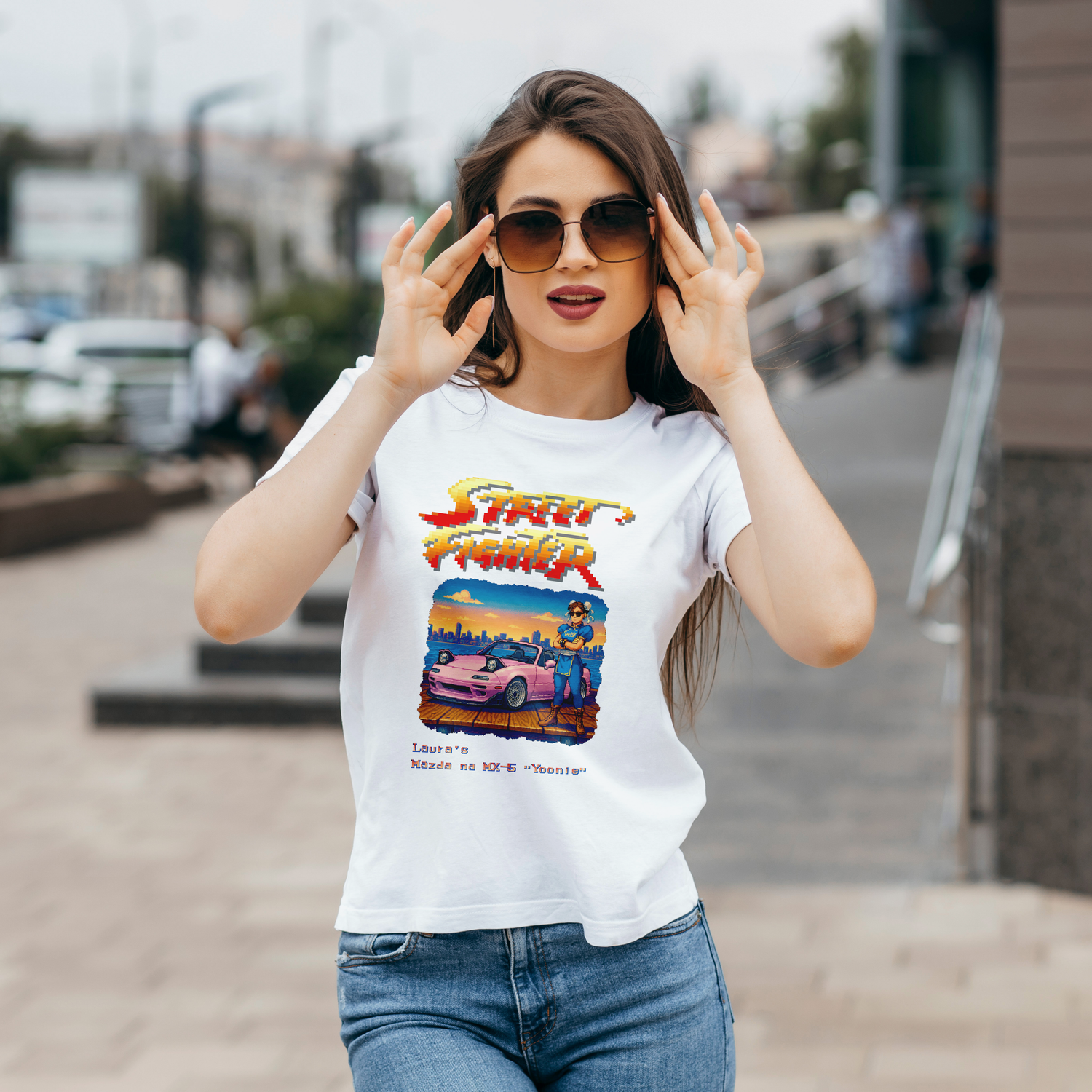 Young brunette lady shows off her custom mad white T-shirt featuring her likeness in Chun Li dress, standing in front of her pink Mazda MX-5. Inspired by Street Fighter II's bonus stage