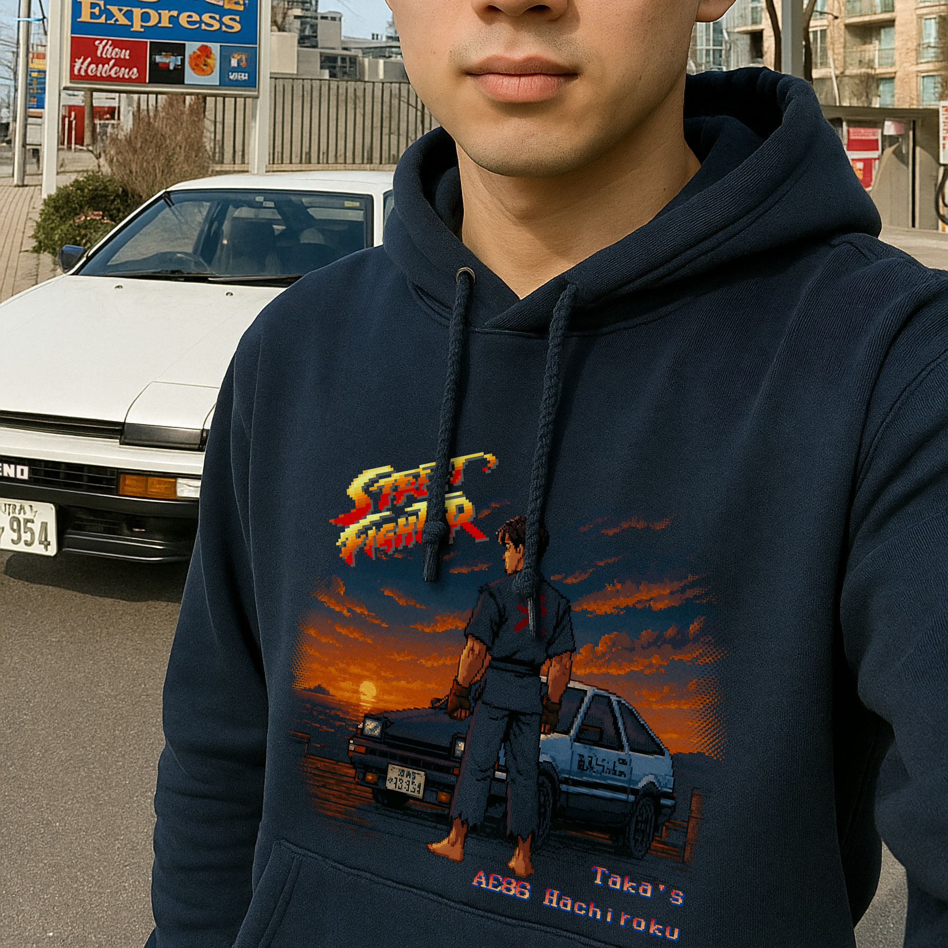 Navy hoodie featuring a retro 16-bit Street Fighter II–style pixel art scene of 'Taka' standing Akuma-style with his AE86 Trueno at sunrise on a dock. The iconic car sports the Fujiwara Tofu Shop livery and authentic Japanese license plate, set against a moody skyline that fades into the hoodie fabric. A tribute to drifting legends and pixel-perfect nostalgia.