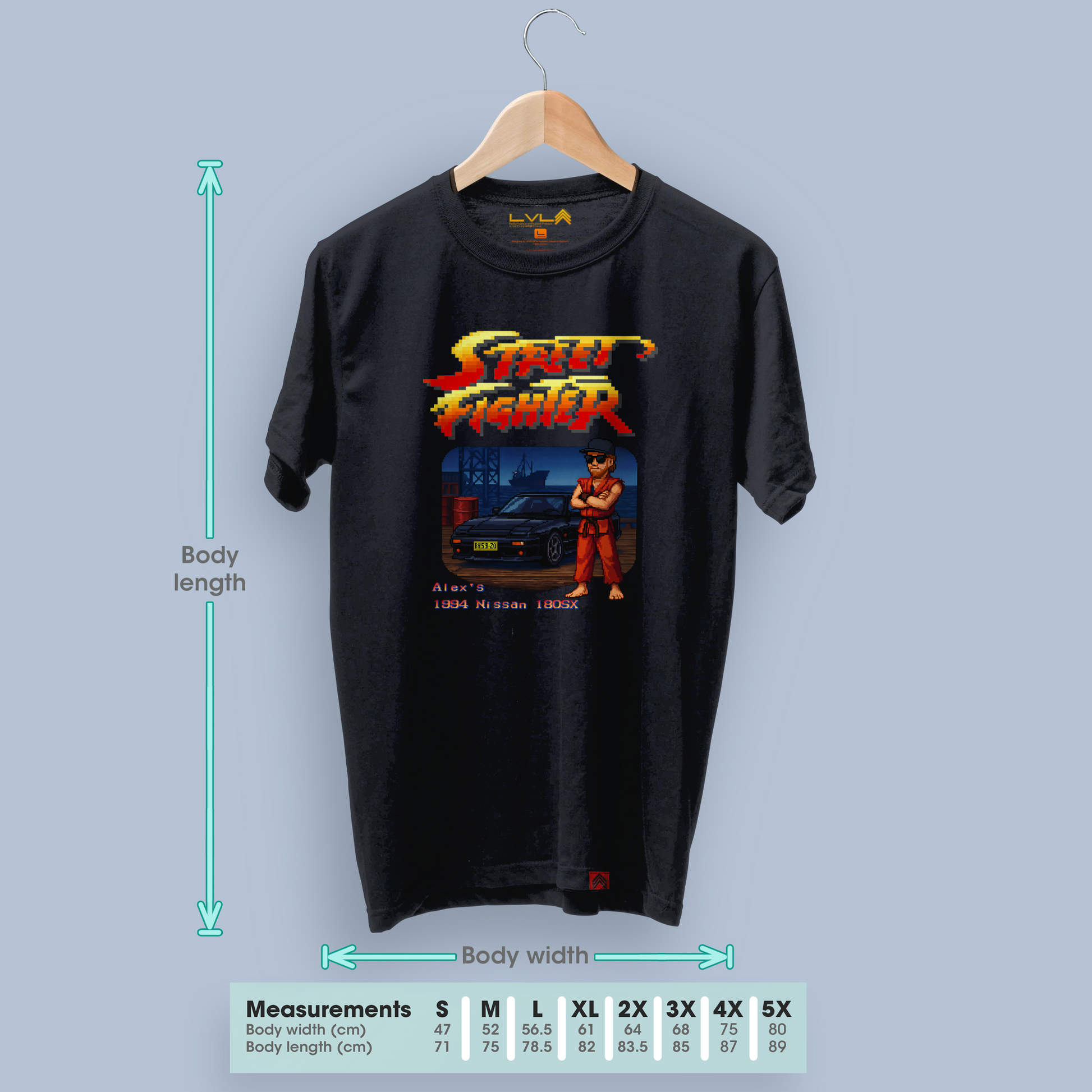 Black t-shirt with custom Street Fighter-style pixel art hanging on a coathanger against a blank wall, displayed next to a size chart for measurements.